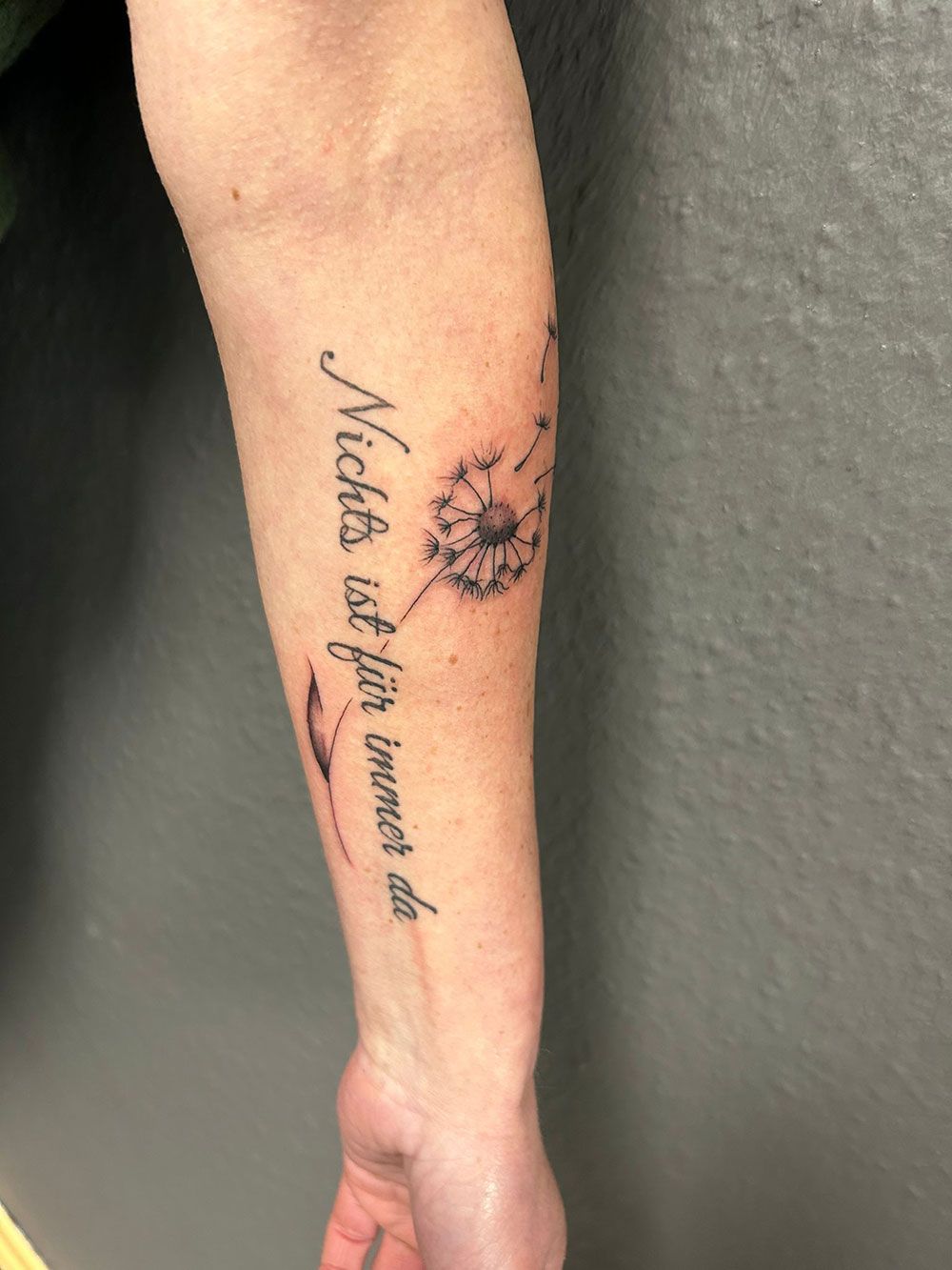 Eine Person hat eine Löwenzahntätowierung auf dem Unterarm