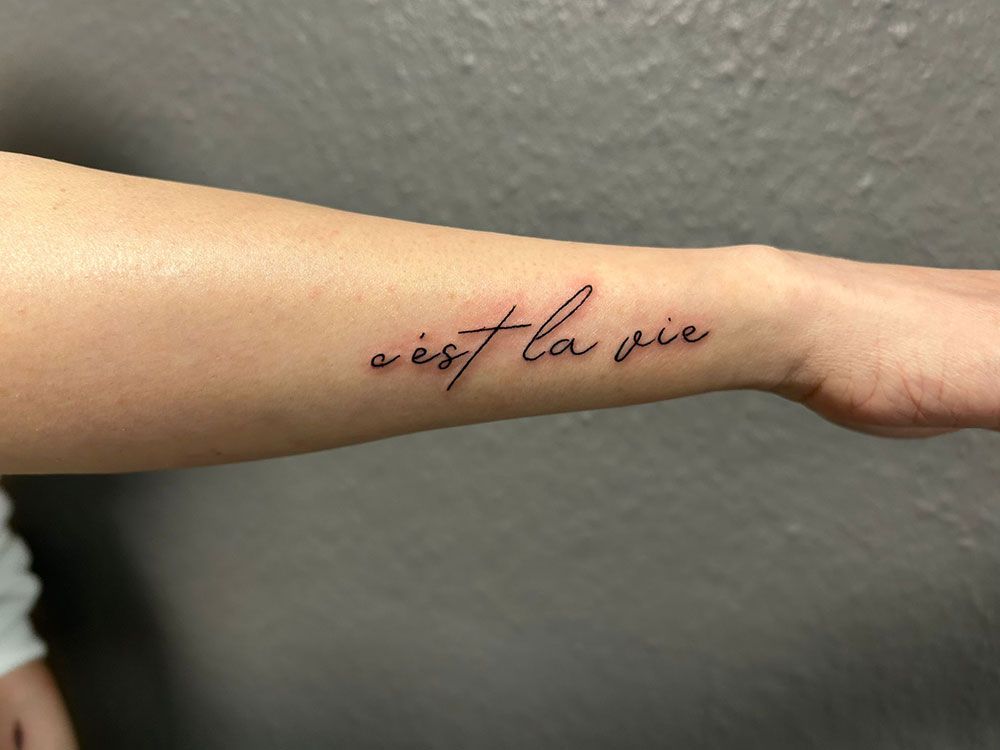 Eine Person hat ein Tattoo am Handgelenk mit der Aufschrift „C’est la vie“