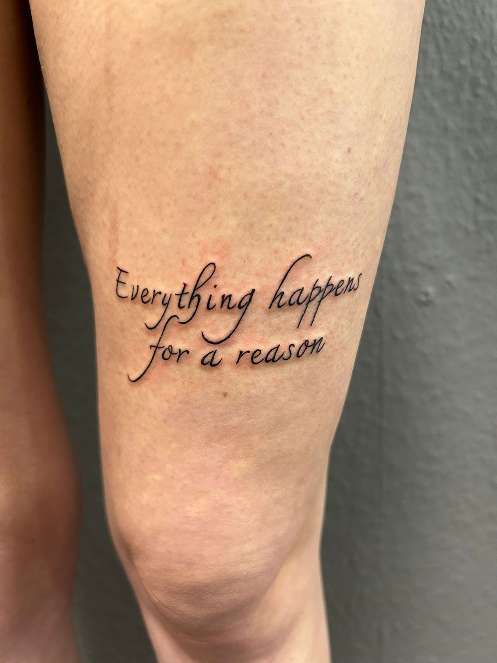 Eine Frau hat eine Tätowierung auf ihrem Bein mit der Aufschrift „Alles geschieht aus einem bestimmten Grund“.