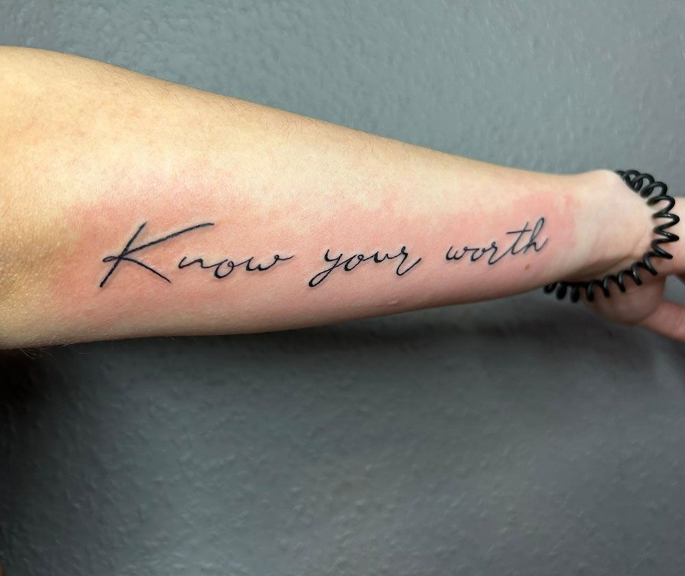 Eine Person hat eine Tätowierung auf dem Unterarm mit der Aufschrift „Kenne deinen Wert“.