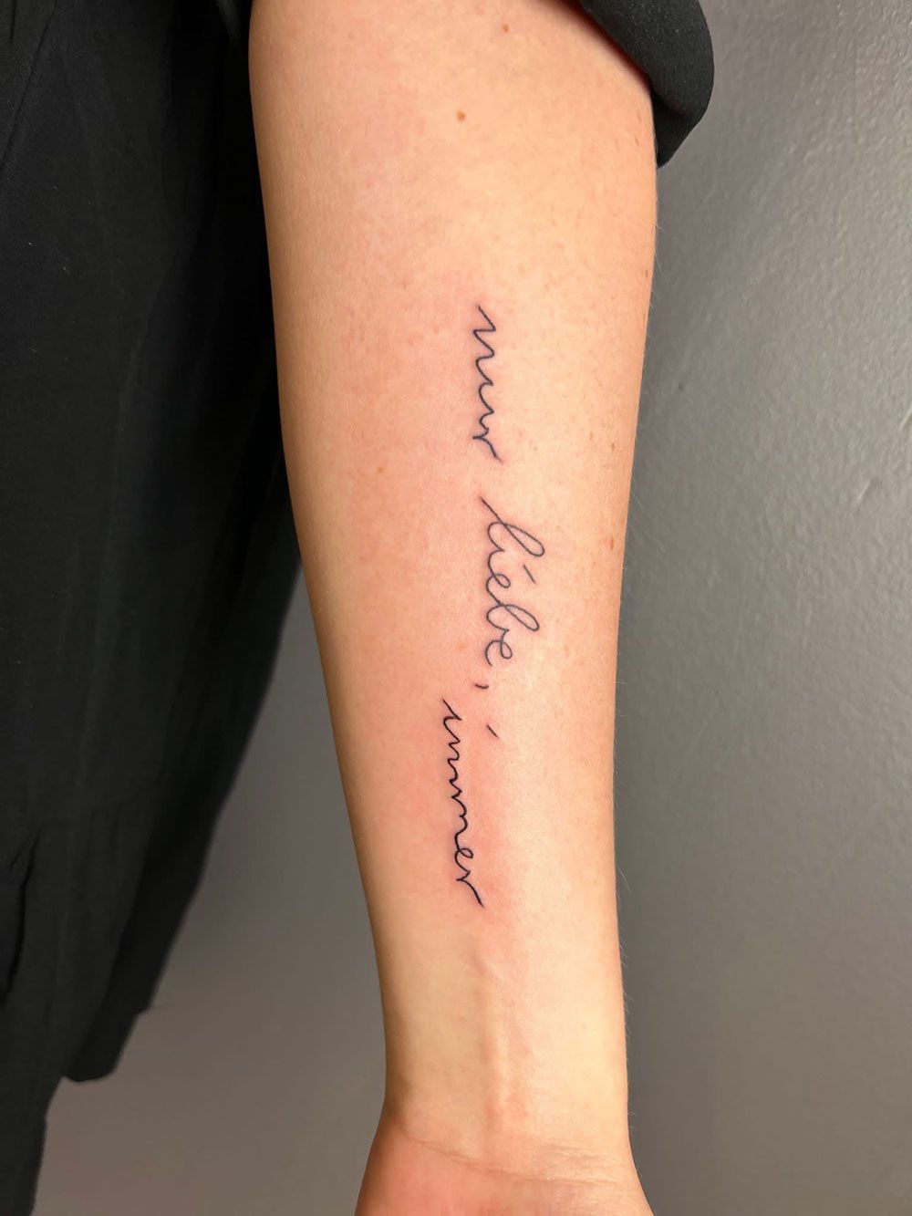 Eine Frau hat eine Tätowierung auf ihrem Unterarm mit der Aufschrift „Pour l' amour“.