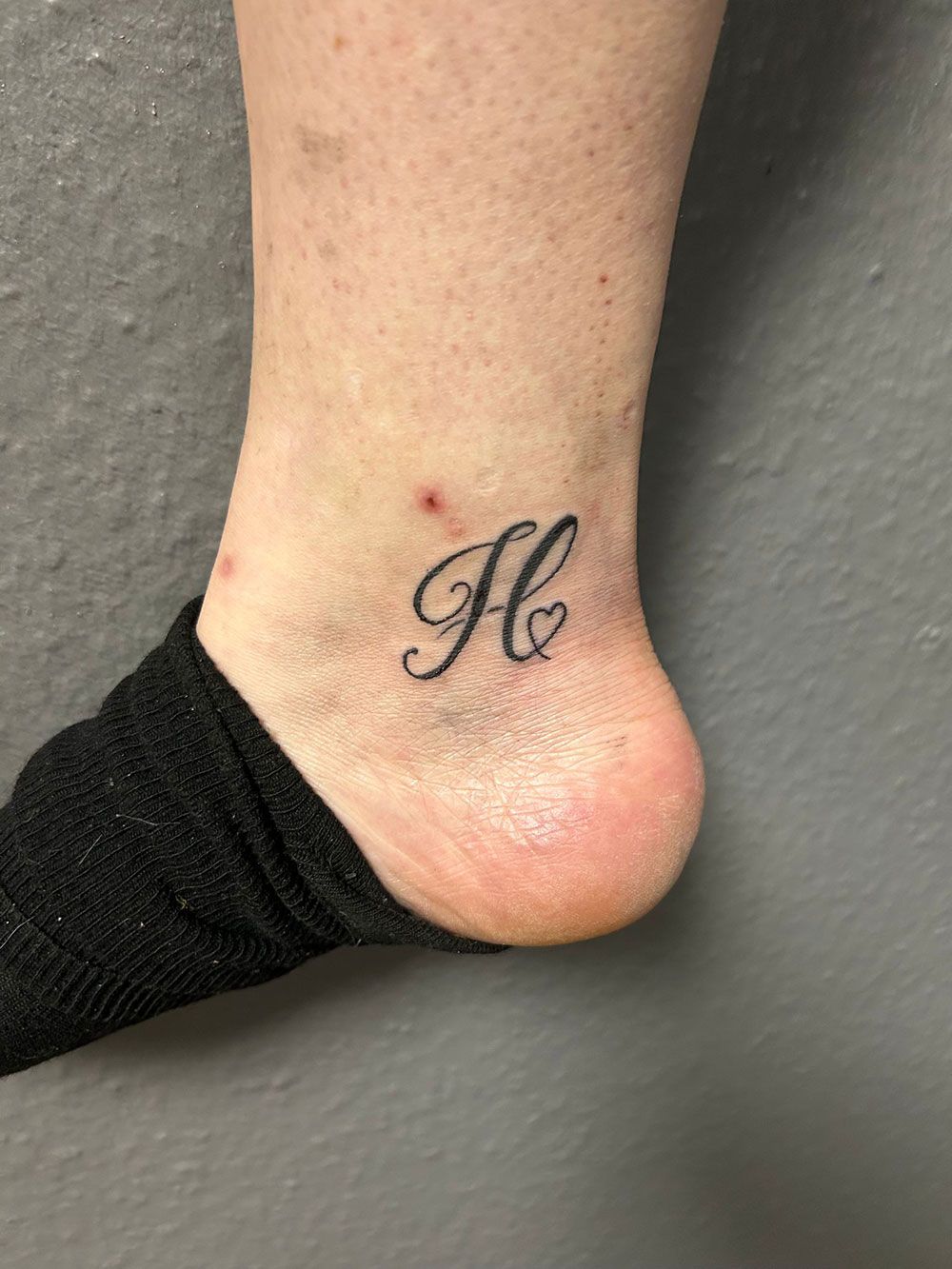 Eine Person hat eine Tätowierung mit dem Buchstaben H auf ihrem Knöchel.
