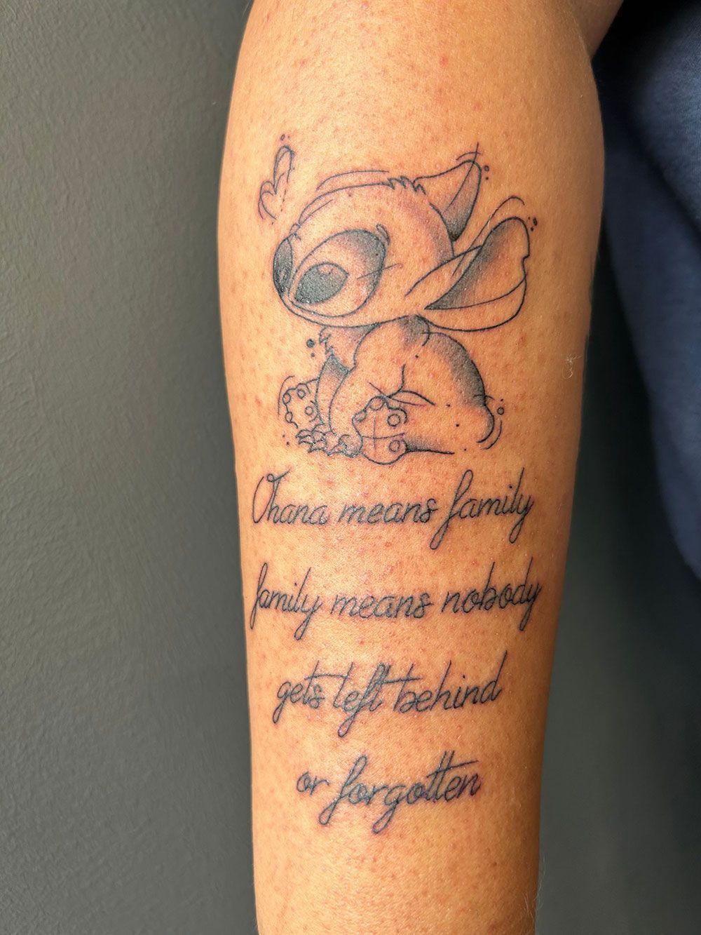 Ein Tattoo auf dem Arm einer Person mit der Aufschrift „Ohana“ bedeutet Familie
