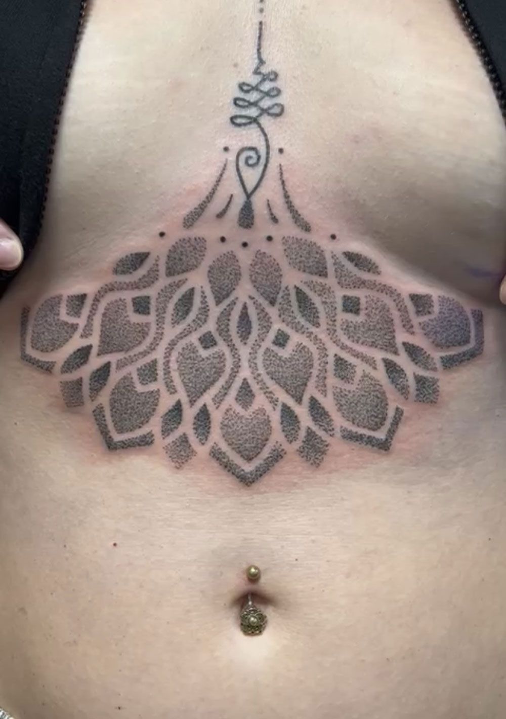 Eine Frau hat eine Tätowierung auf der Brust, die wie ein Kronleuchter aussieht.