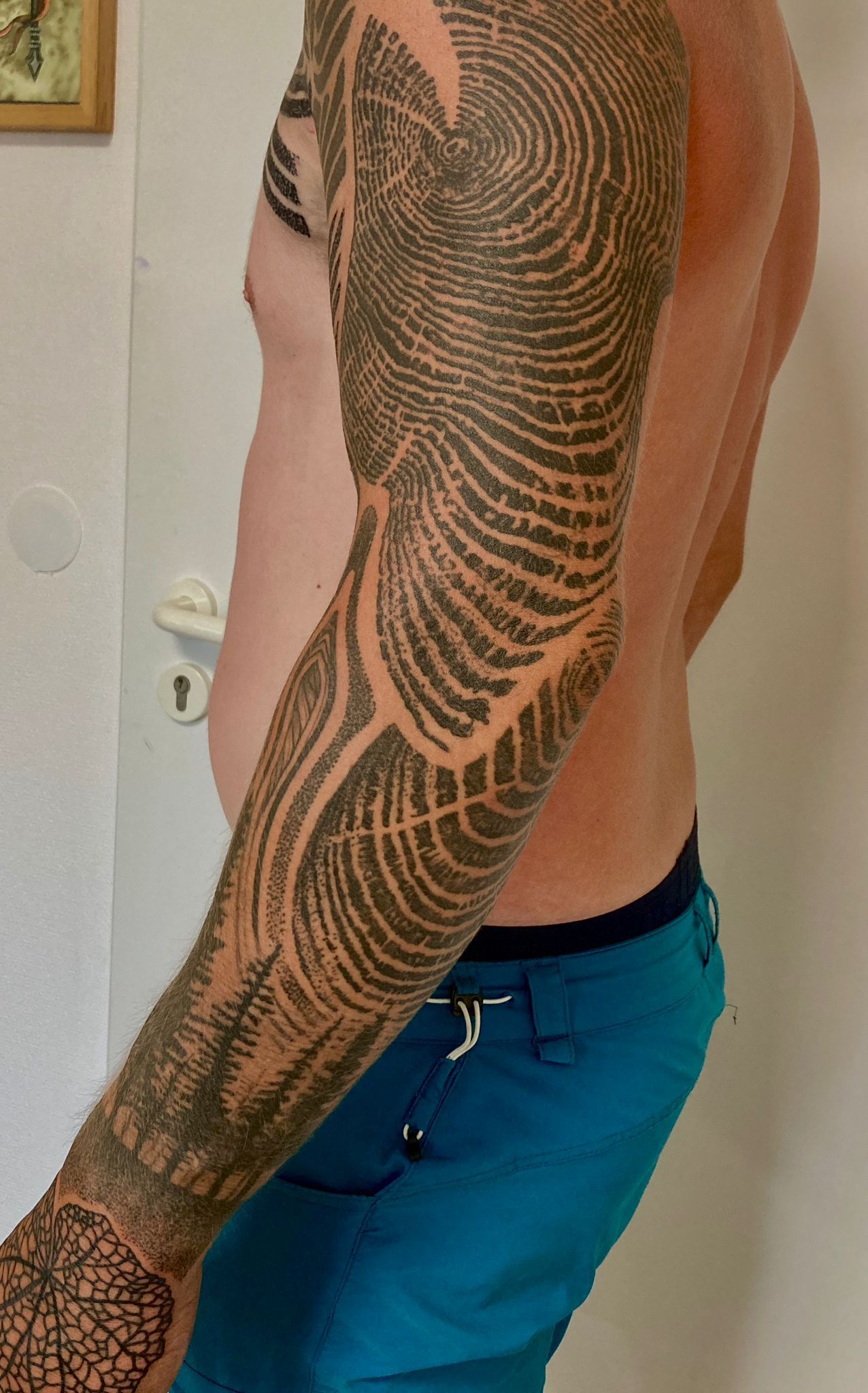 Ein Mann mit einer Tätowierung auf dem Arm steht vor einer Tür.