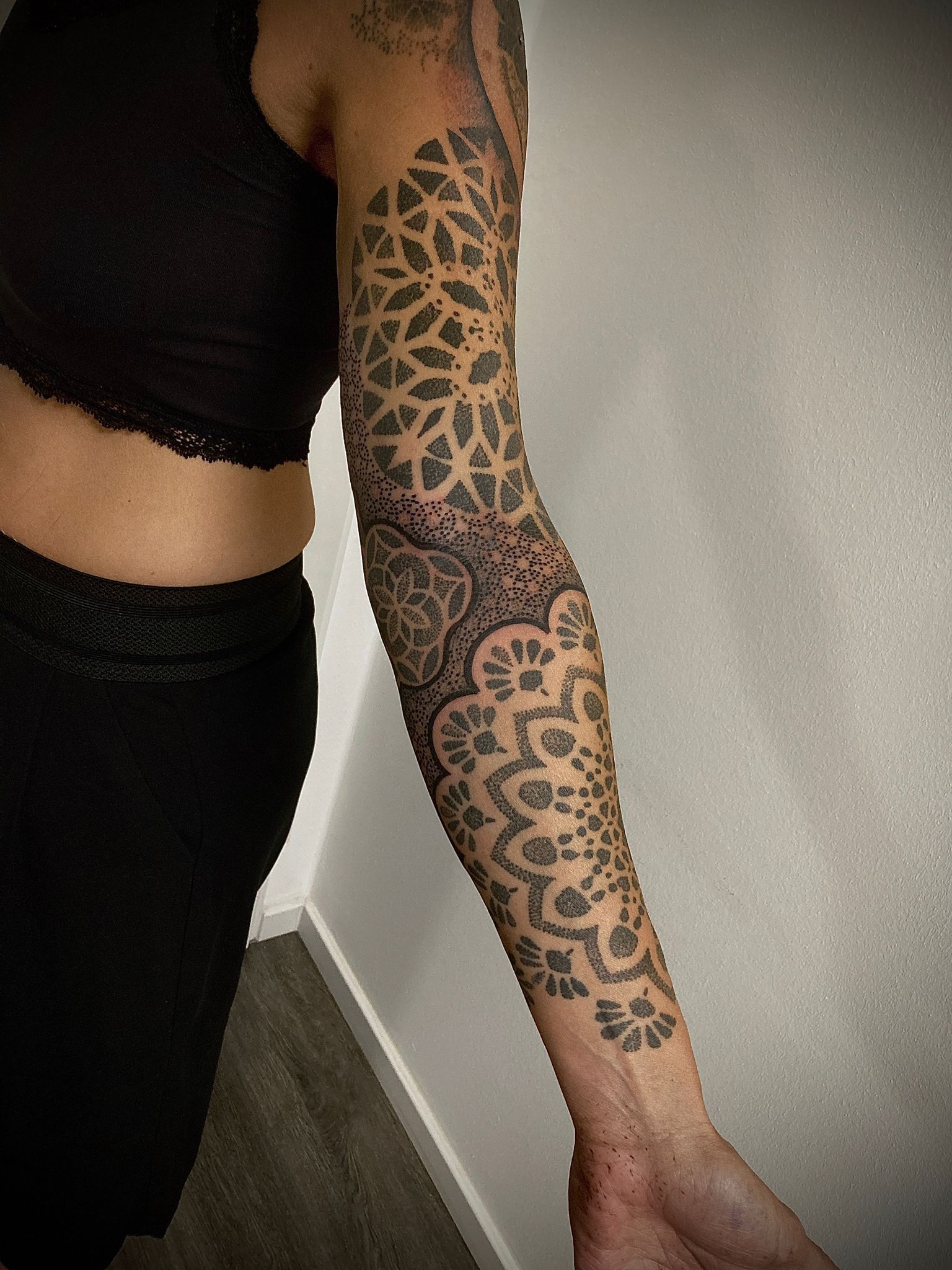 Eine Frau mit einer Tätowierung auf dem Arm steht neben einer Wand.