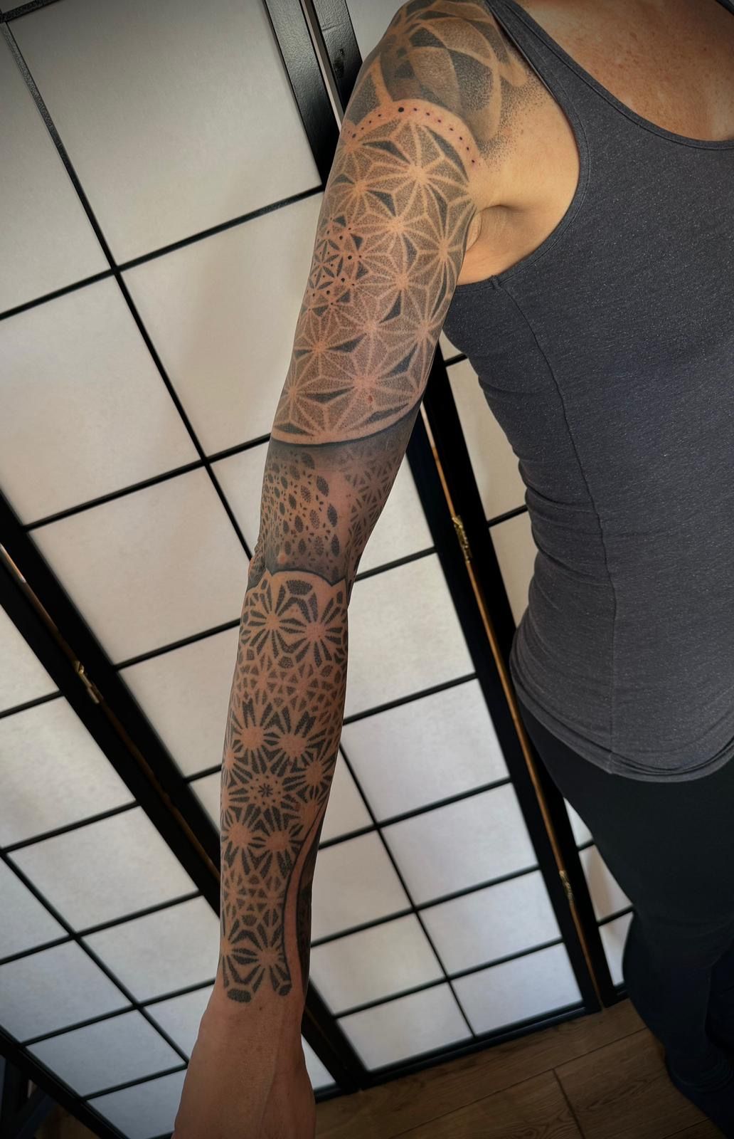 Eine Frau mit einem Tattoo auf dem Arm trägt ein graues Tanktop