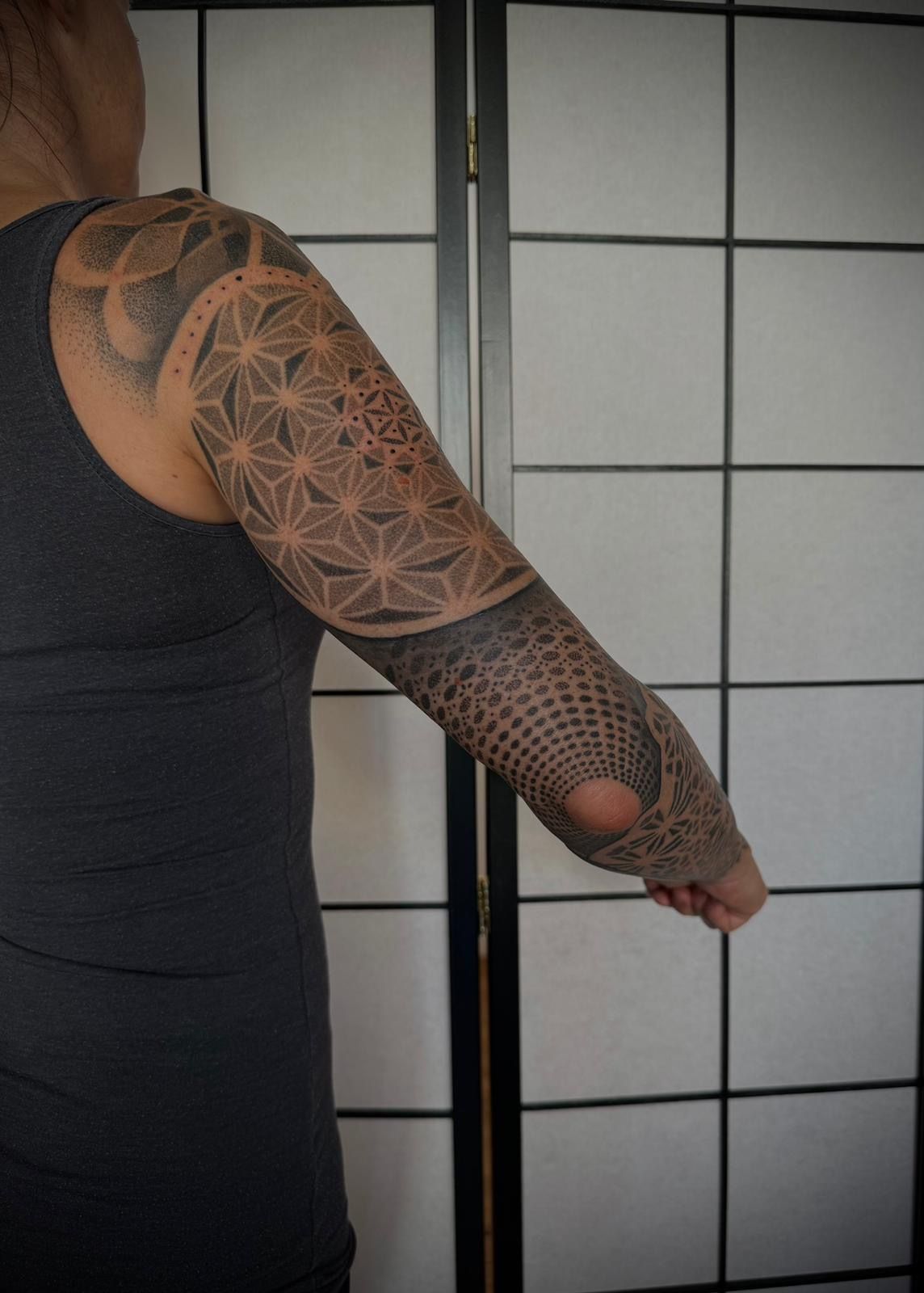 Ein Mann mit einer Tätowierung auf dem Arm steht vor einem Bildschirm.