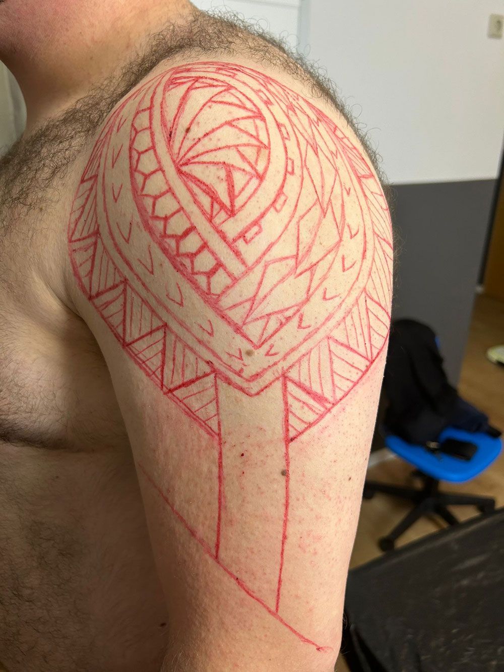 Ein Mann ohne Hemd hat eine rote Tätowierung auf seiner Schulter.