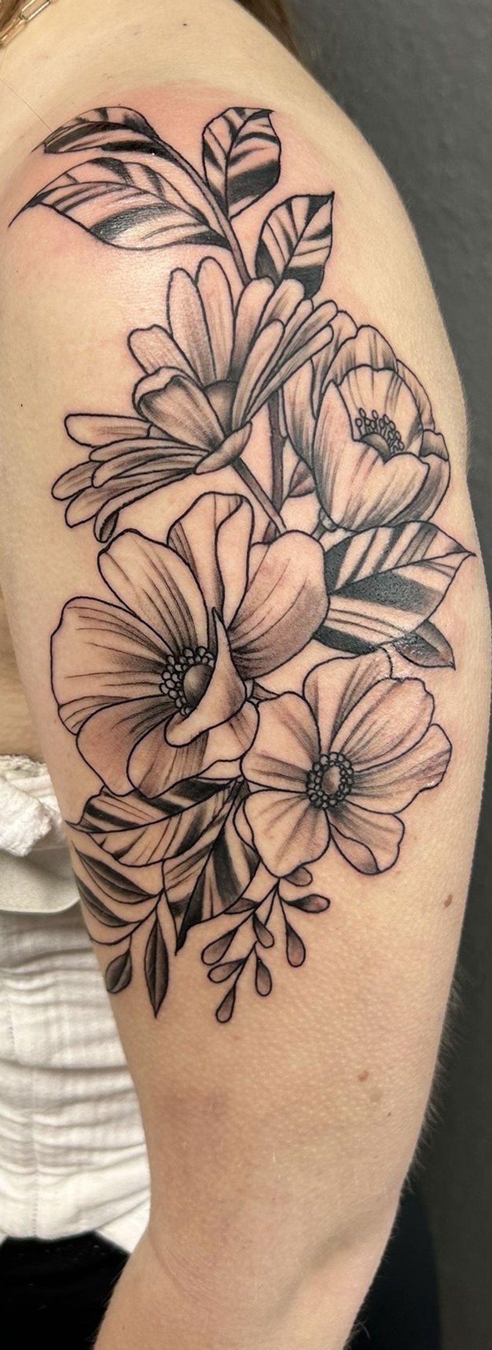 Eine Frau hat eine Tätowierung mit Blumen und Blättern auf ihrer Schulter.