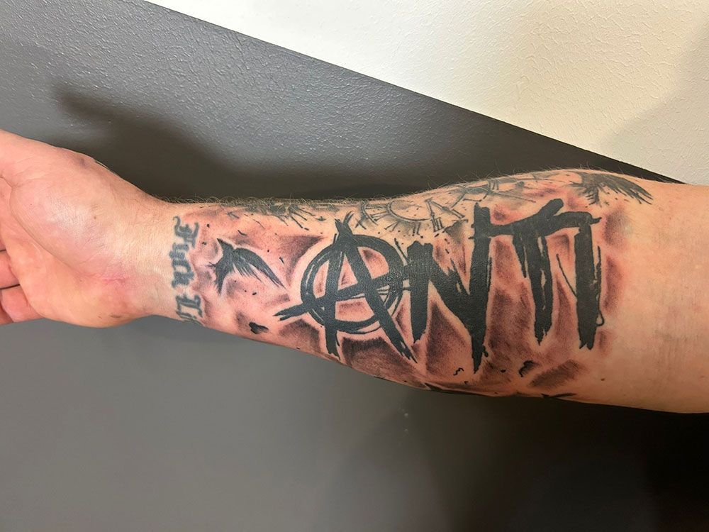 Ein Mann hat ein Tattoo auf seinem Unterarm mit der Aufschrift „Anti