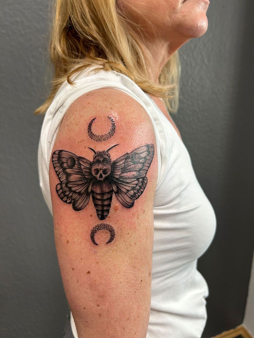 Eine Frau hat eine Tätowierung einer Motte und einer Mondsichel auf ihrem Arm.