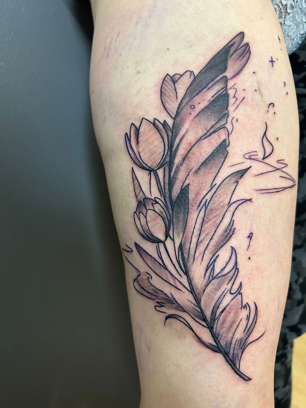 Eine Person hat eine Tätowierung einer Feder mit Blumen auf ihrem Bein.