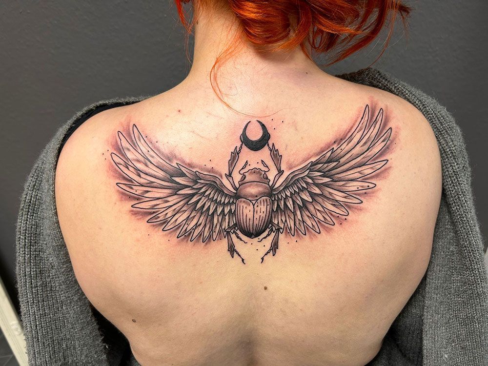 Eine Frau hat eine Tätowierung eines Skarabäus mit Flügeln auf ihrem Rücken.