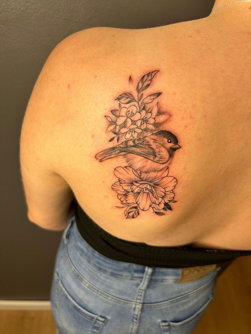Eine Frau hat eine Tätowierung mit einem Vogel und Blumen auf ihrem Rücken.