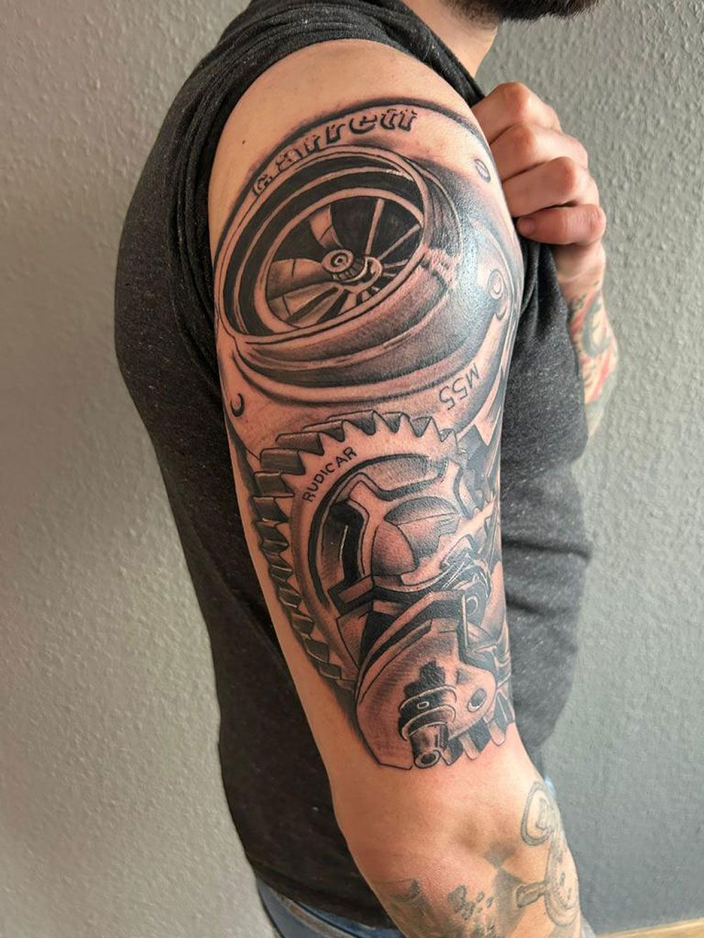 Ein Mann hat eine Tätowierung mit einem Rad und einem Zahnrad auf seinem Arm.