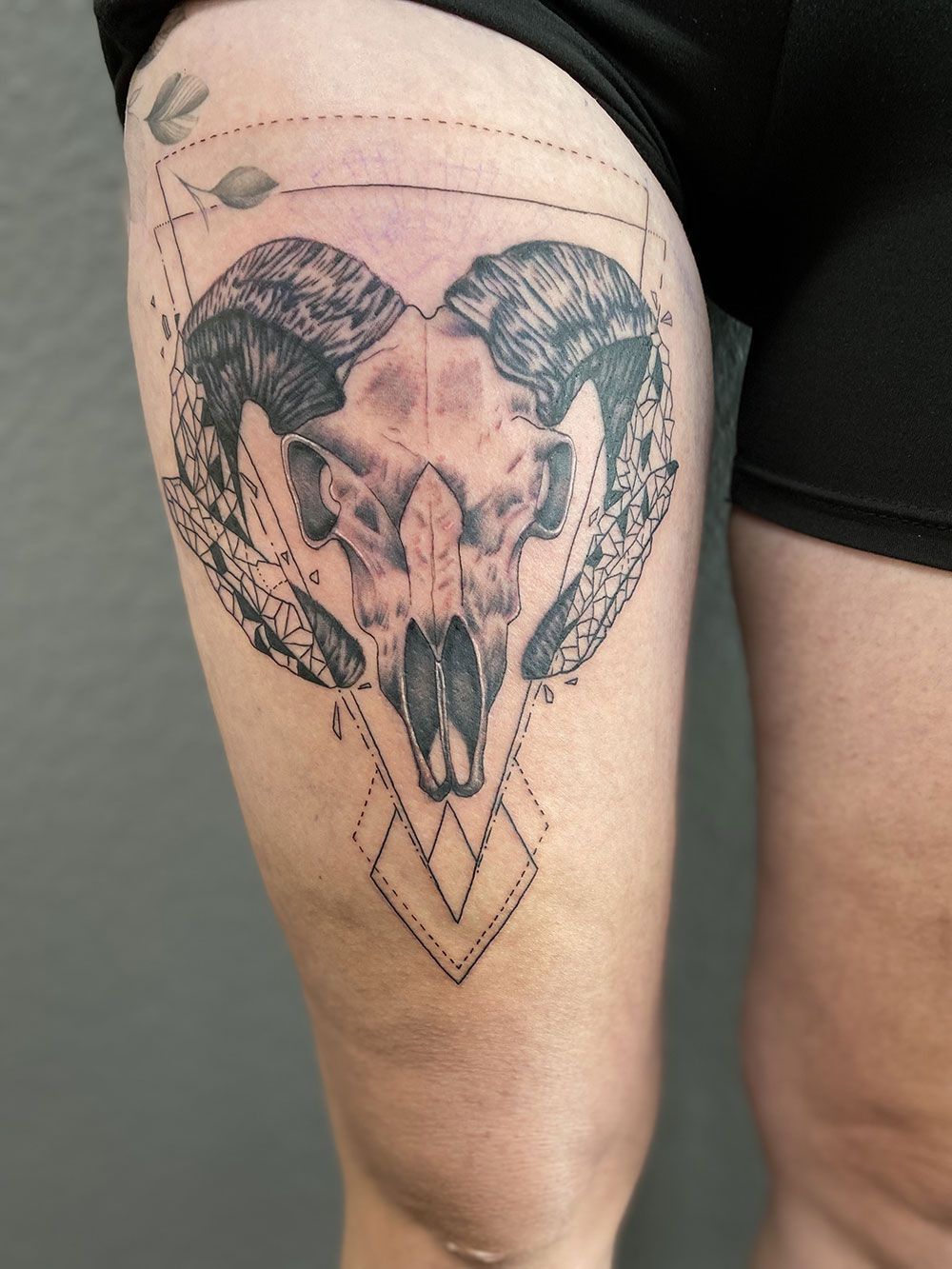 Eine Frau hat ein Tattoo mit einem Widderschädel auf ihrem Oberschenkel