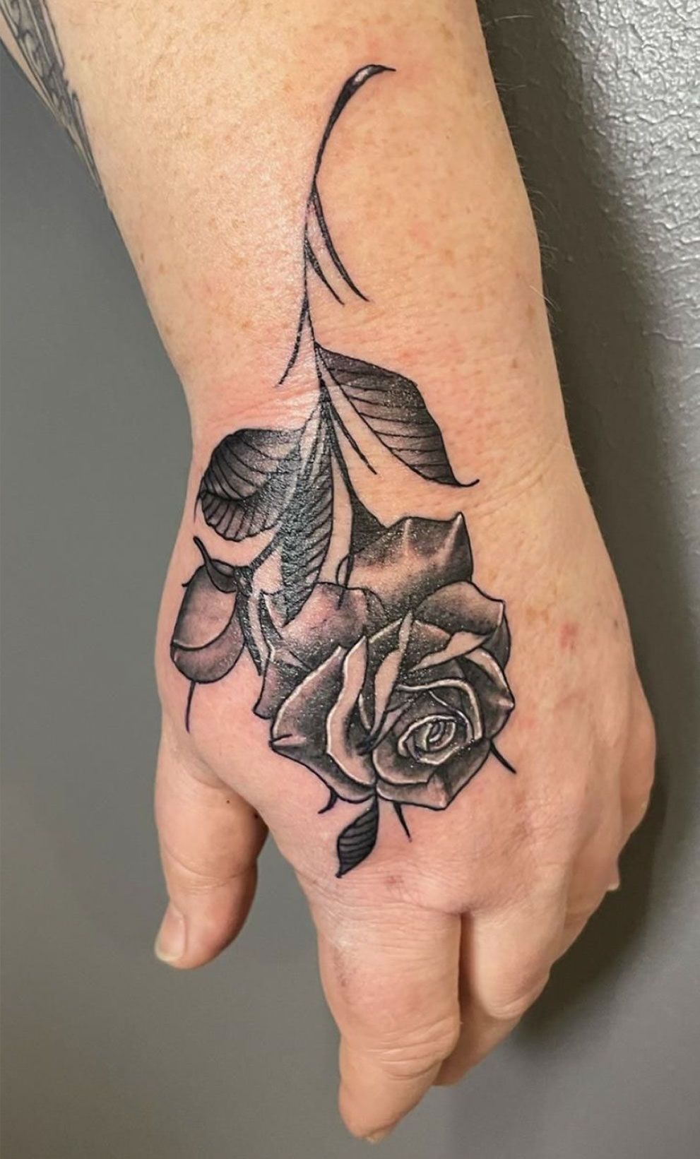 Eine Person hat eine schwarz-weiße Tätowierung einer Rose auf der Hand.