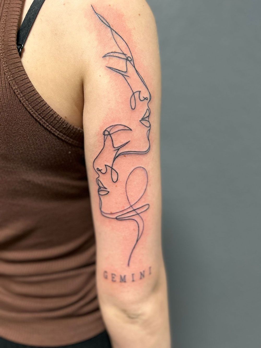 Eine Frau hat eine Tätowierung mit zwei Gesichtern auf ihrem Arm.