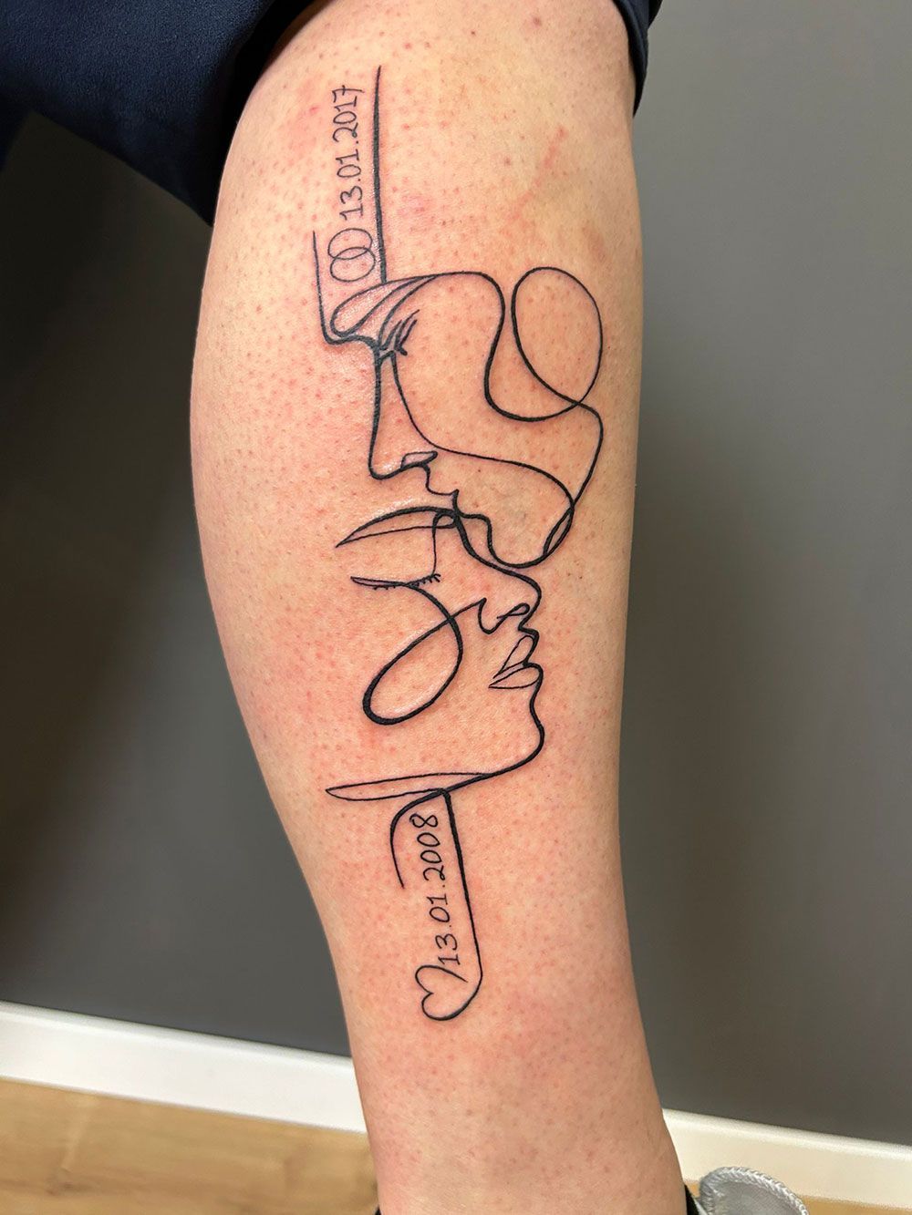 Eine Person hat eine Tätowierung mit den Gesichtern eines Paares auf ihrem Bein.