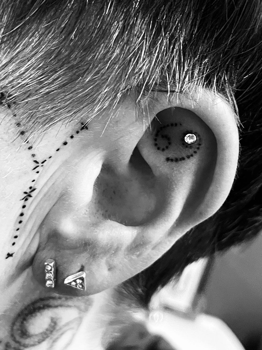 Ein Schwarzweißfoto des Ohrs einer Person mit einer Krebstätowierung darauf.