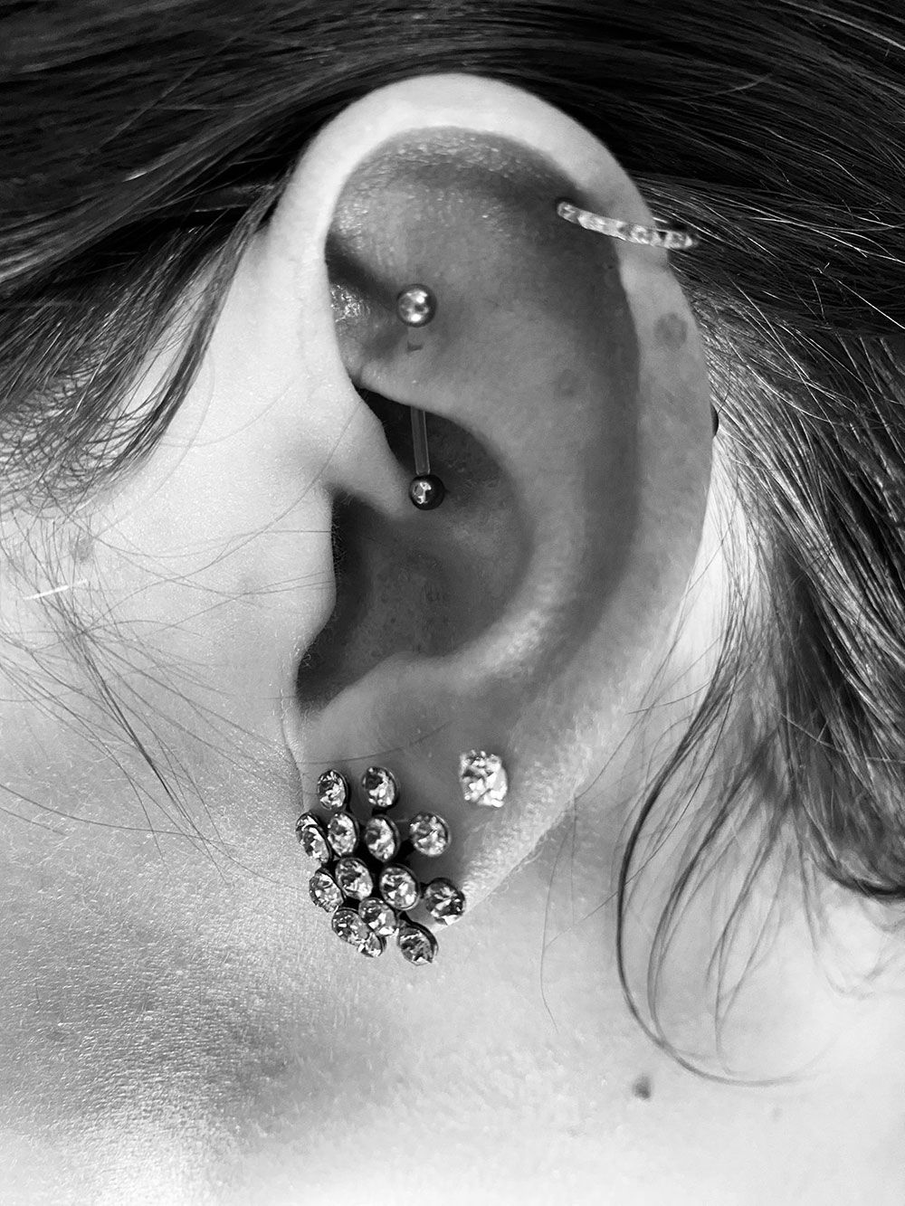 Ein Schwarzweißfoto des Ohrs einer Frau mit mehreren Piercings.