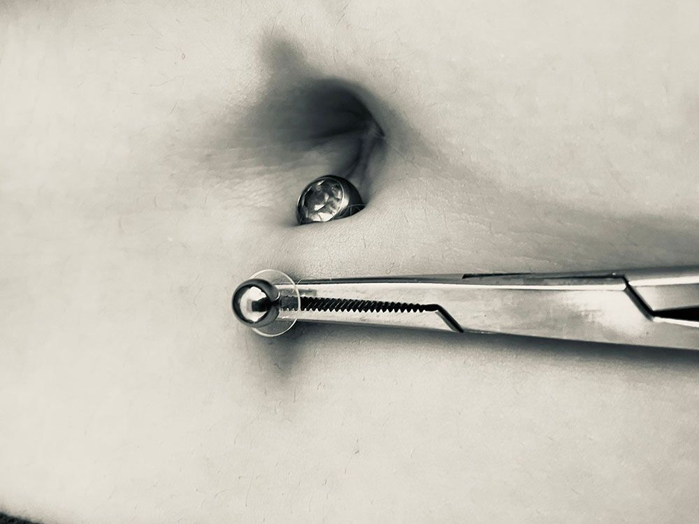 Einer Person wird mit einer Zange der Bauchnabel gepierct.