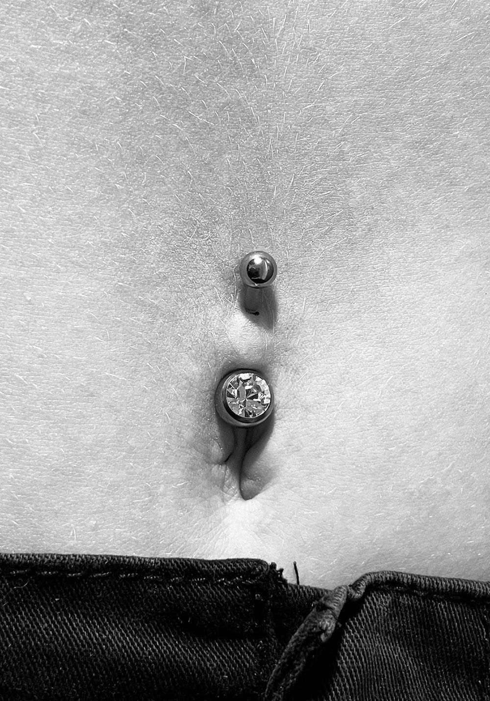Ein Schwarzweißfoto vom Bauch einer Frau mit einem Bauchnabelpiercing.