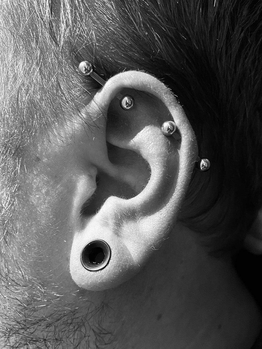 Ein Schwarzweißfoto des Ohrs eines Mannes mit mehreren Piercings.