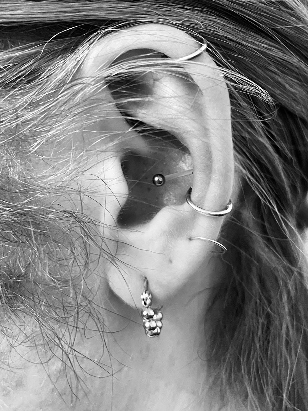 Ein Schwarzweißfoto des Ohrs einer Frau mit mehreren Piercings.