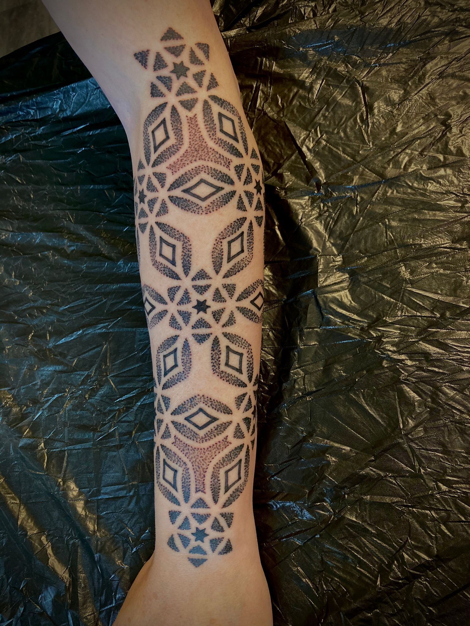Eine Person hat eine Tätowierung auf dem Arm, die wie ein Kreuzstichmuster aussieht.