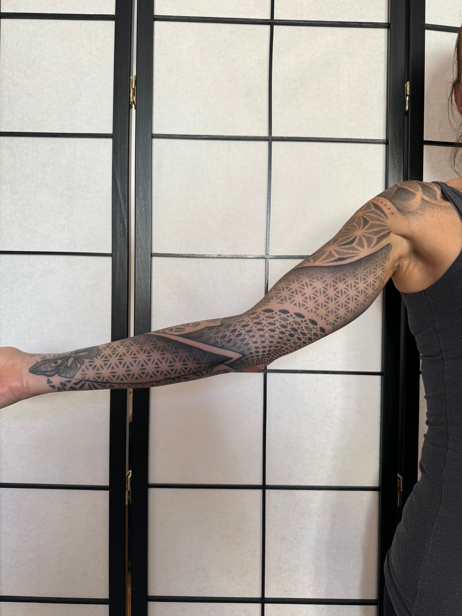 Eine Frau mit einer Tätowierung auf dem Arm steht vor einem Bildschirm.