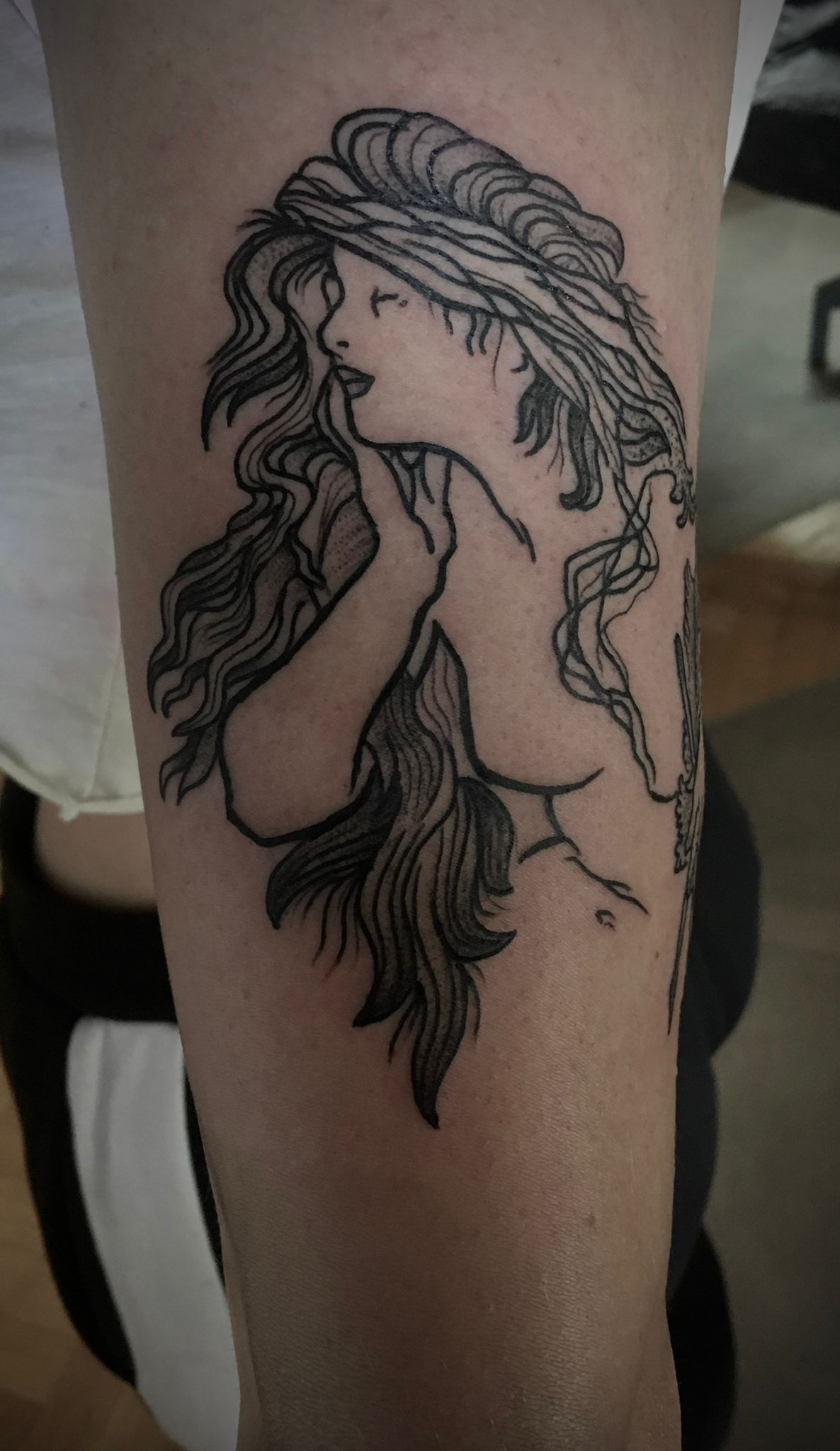 Eine schwarz-weiße Tätowierung einer Frau mit langen Haaren auf dem Arm einer Person.