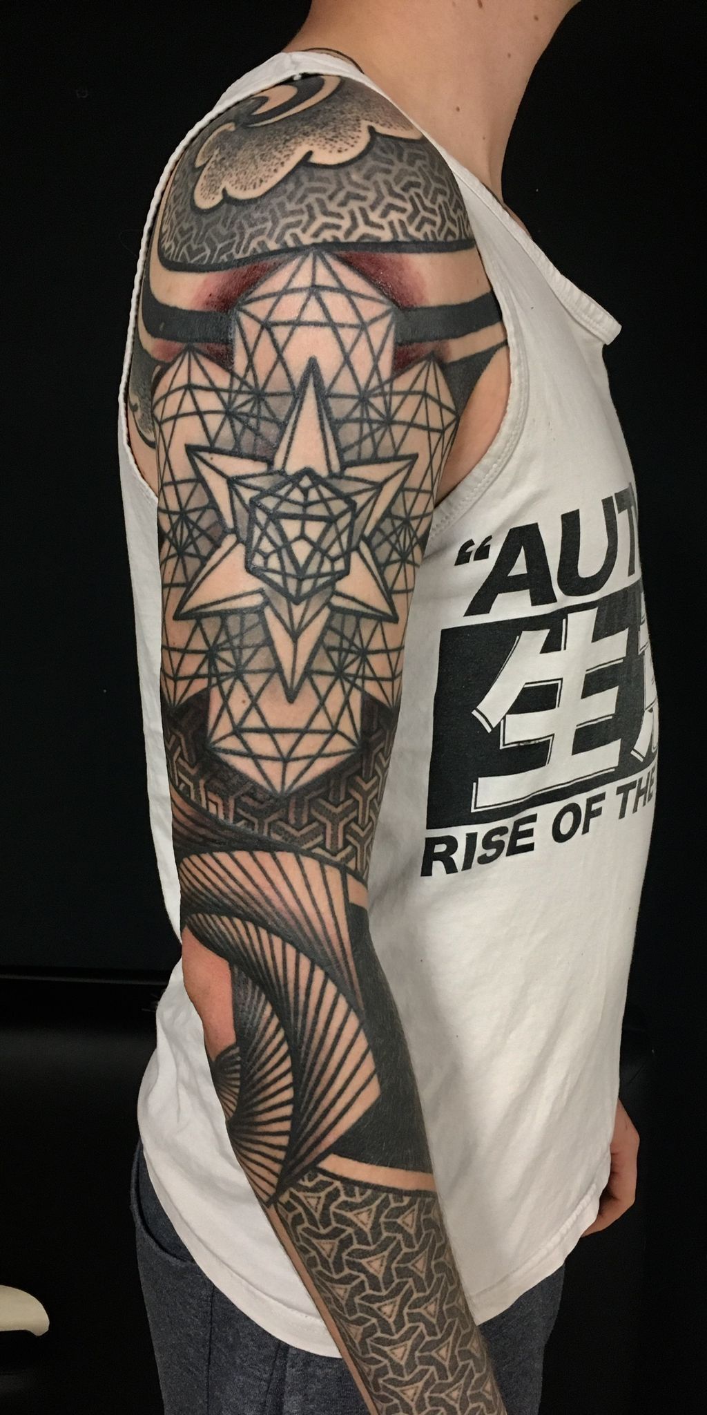 Ein Mann mit einer Tätowierung auf Arm und Schulter trägt ein weißes Tanktop.