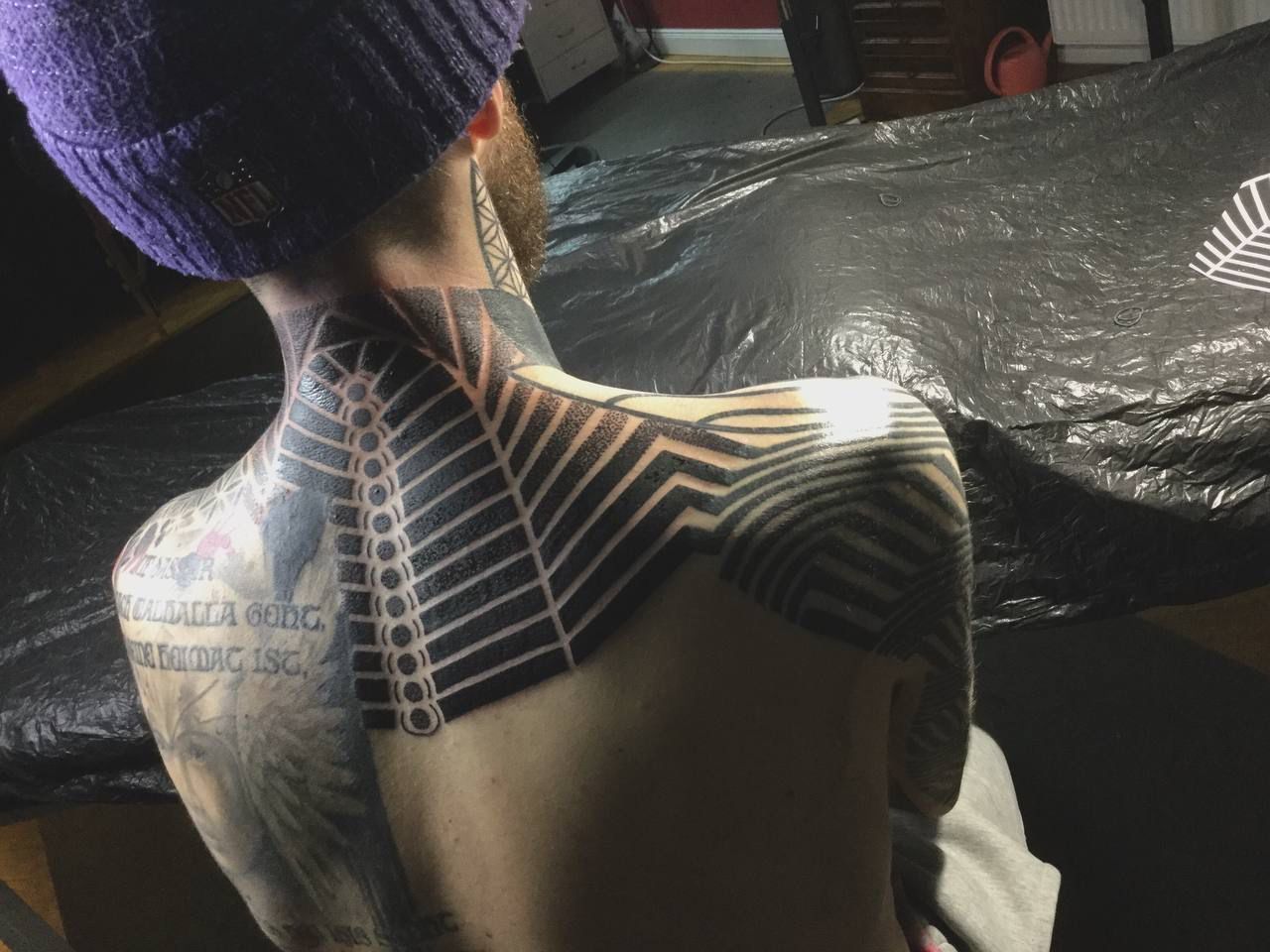 Ein Mann mit einer Tätowierung auf dem Rücken trägt einen lila Hut