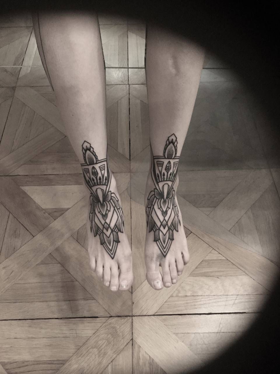 Eine Person mit einer Tätowierung an den Füßen steht auf einem Holzboden.