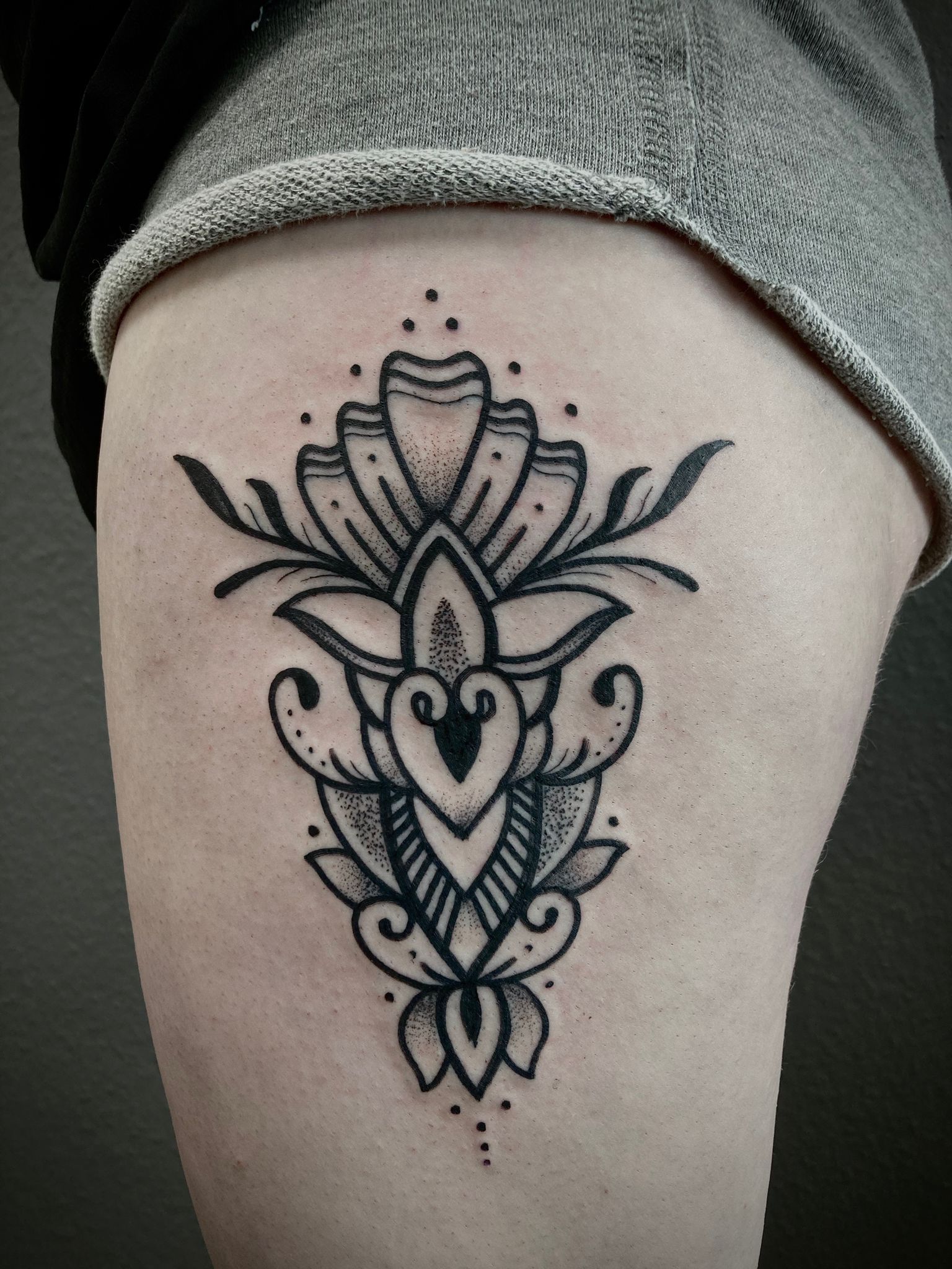 Eine schwarz-weiße Tätowierung einer Blume auf dem Oberschenkel einer Frau.