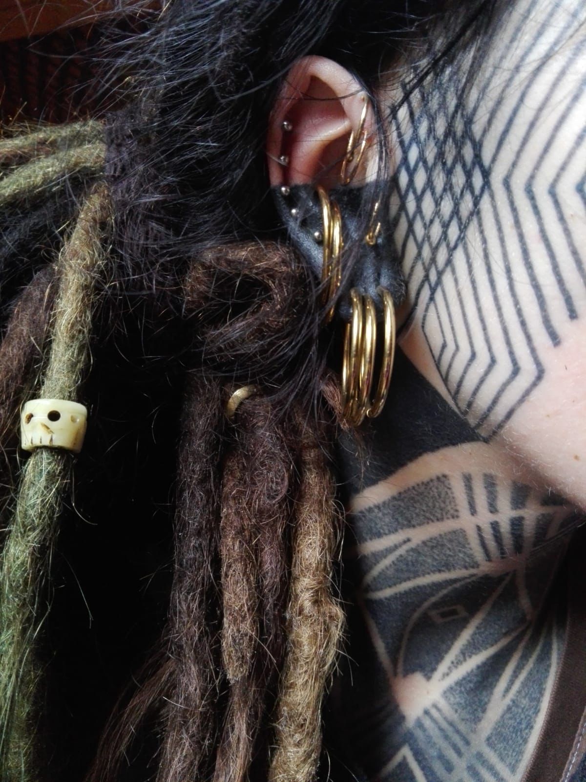 Eine Nahaufnahme vom Ohr einer Person mit Dreadlocks und einer Tätowierung im Gesicht.