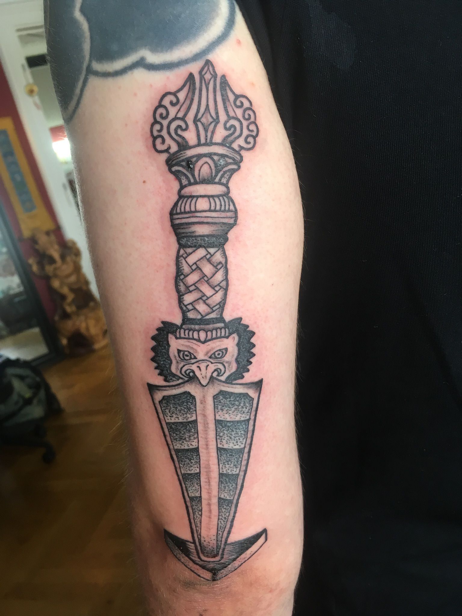 Eine Person hat eine Dolchtätowierung auf dem Arm.