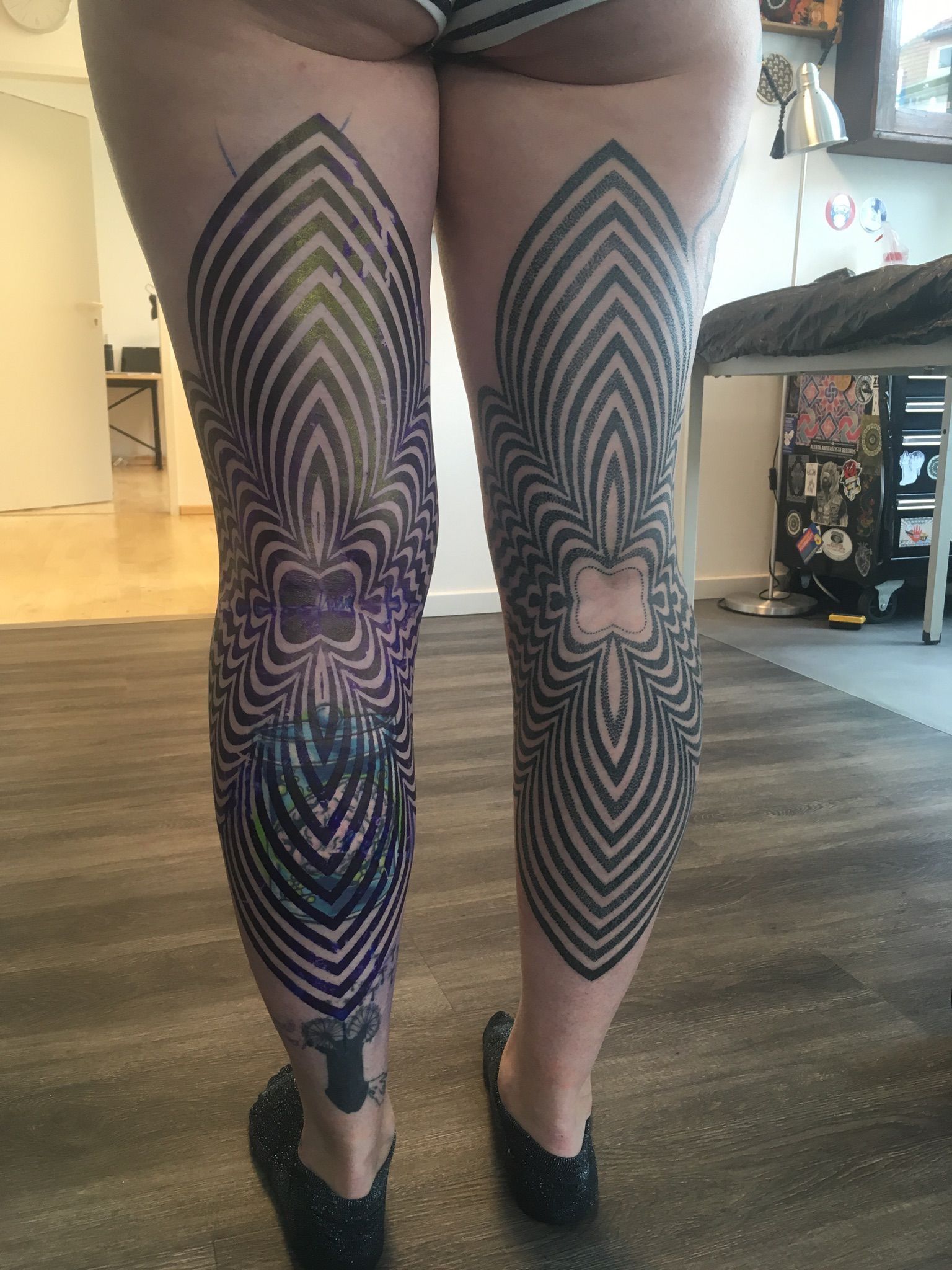 Eine Frau mit einer Tätowierung auf den Beinen steht auf einem Holzboden.