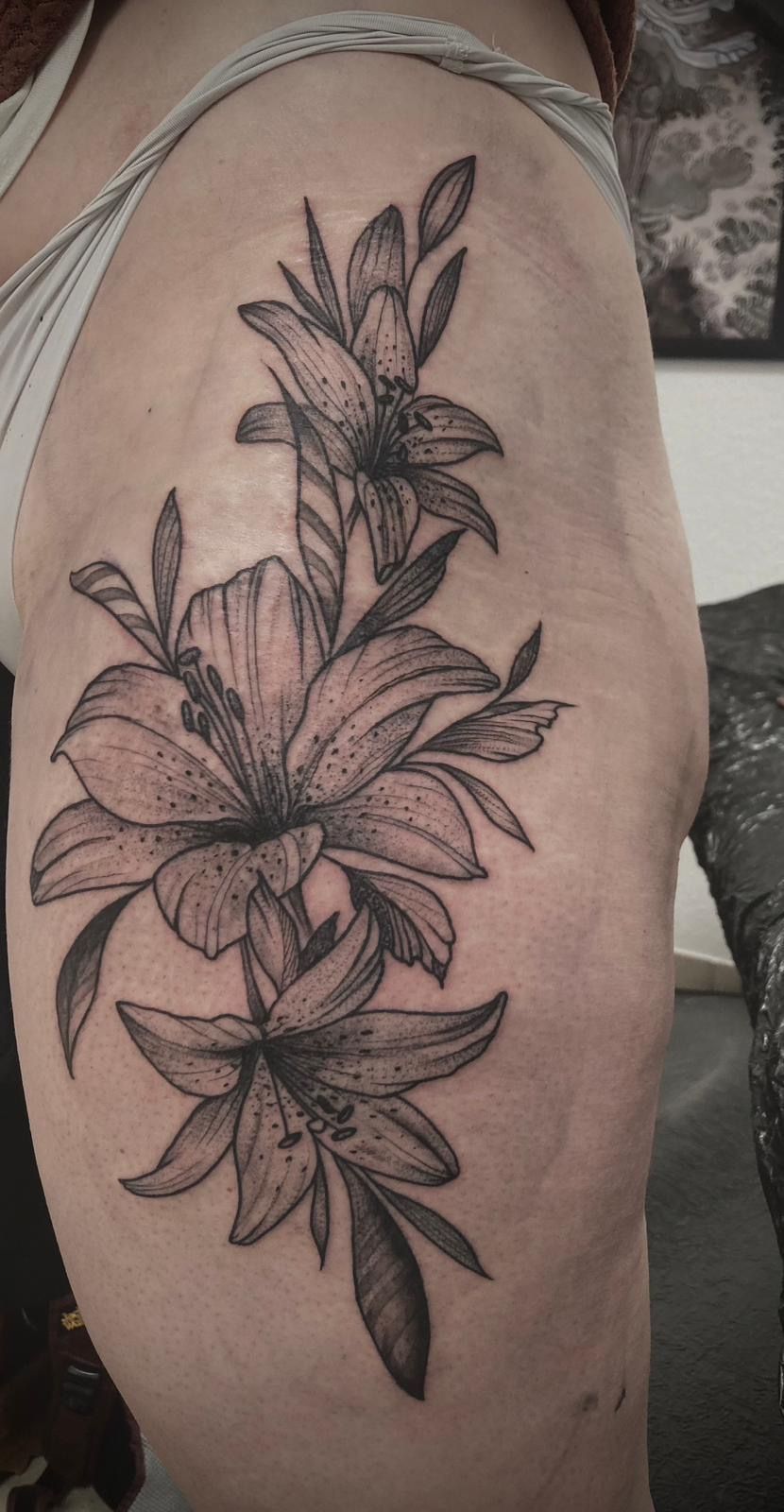 Eine Frau hat eine schwarz-weiße Blumentätowierung auf ihrem Oberschenkel.