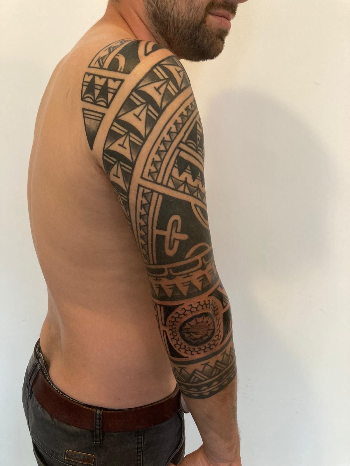 Ein Mann ohne Hemd hat ein Stammestattoo auf seinem Arm.