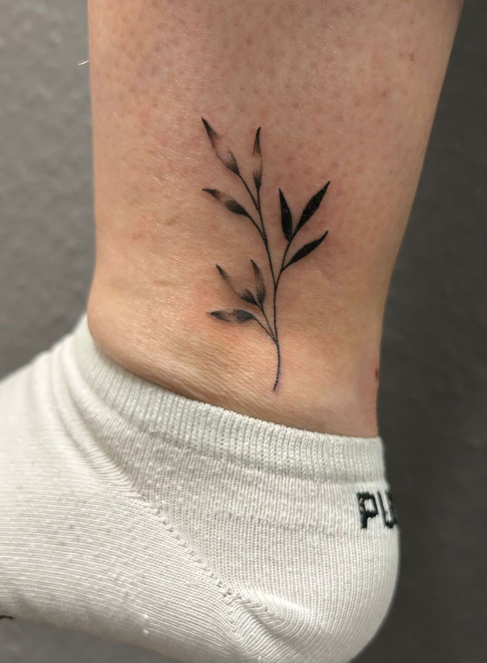 Eine Person hat eine kleine Tätowierung einer Pflanze auf ihrem Knöchel.