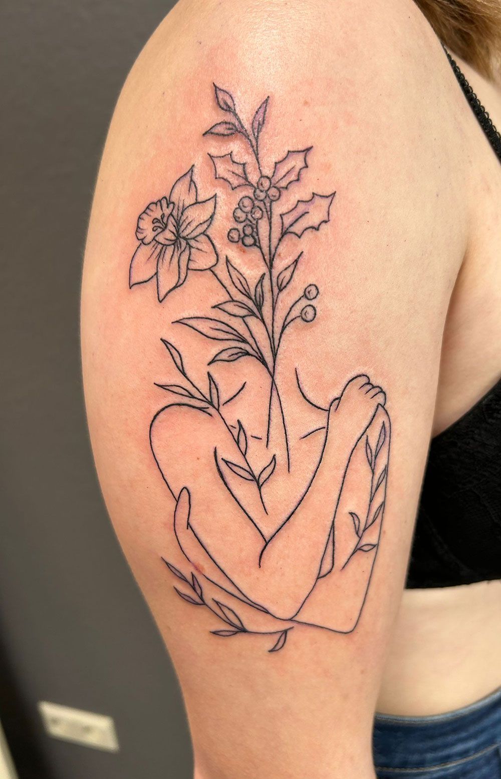 Eine Frau hat eine Tätowierung einer Frau, die Blumen hält, auf ihrem Arm.