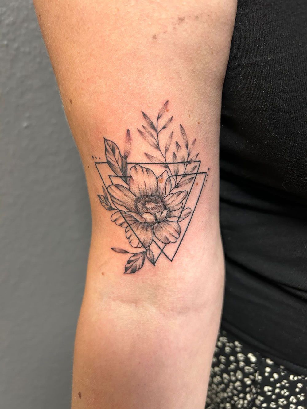 Eine Frau hat eine Tätowierung einer Blume in einem Dreieck auf ihrem Ellbogen