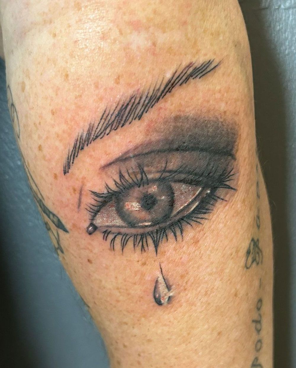 Ein Tattoo eines Frauenauges, aus dem eine Träne herauskommt