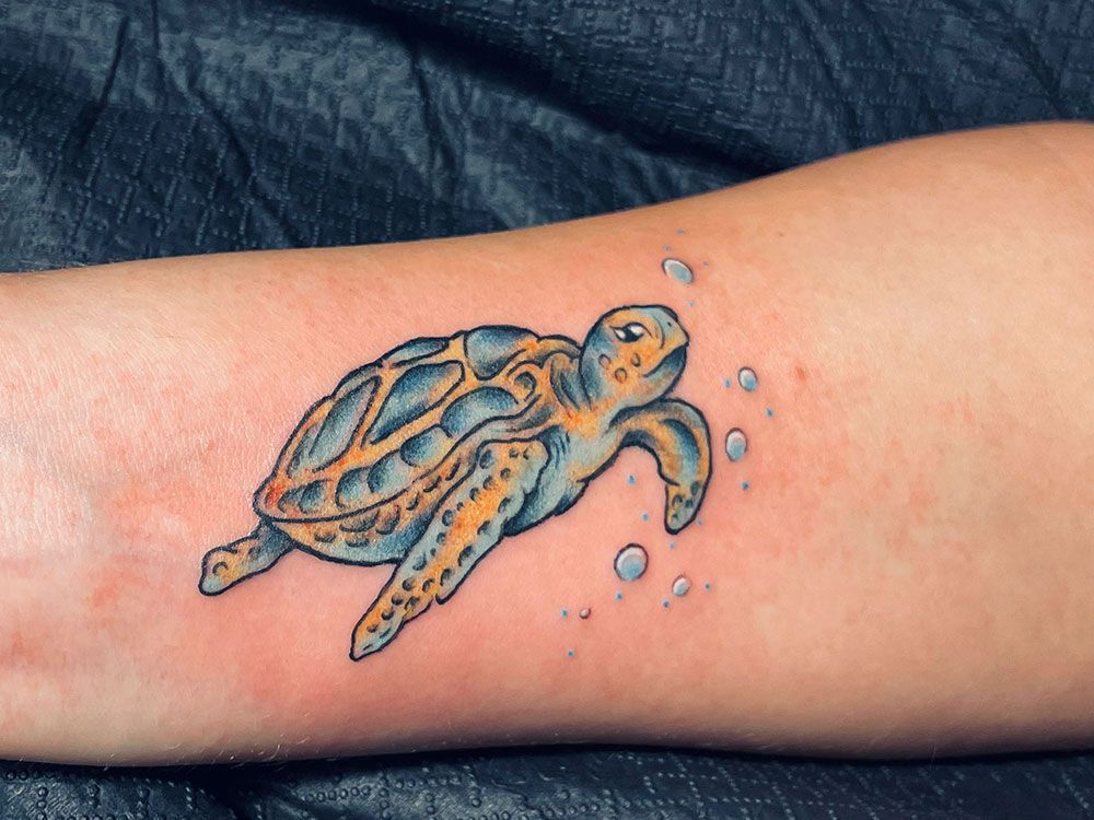Ein Tattoo einer Meeresschildkröte auf dem Arm einer Person
