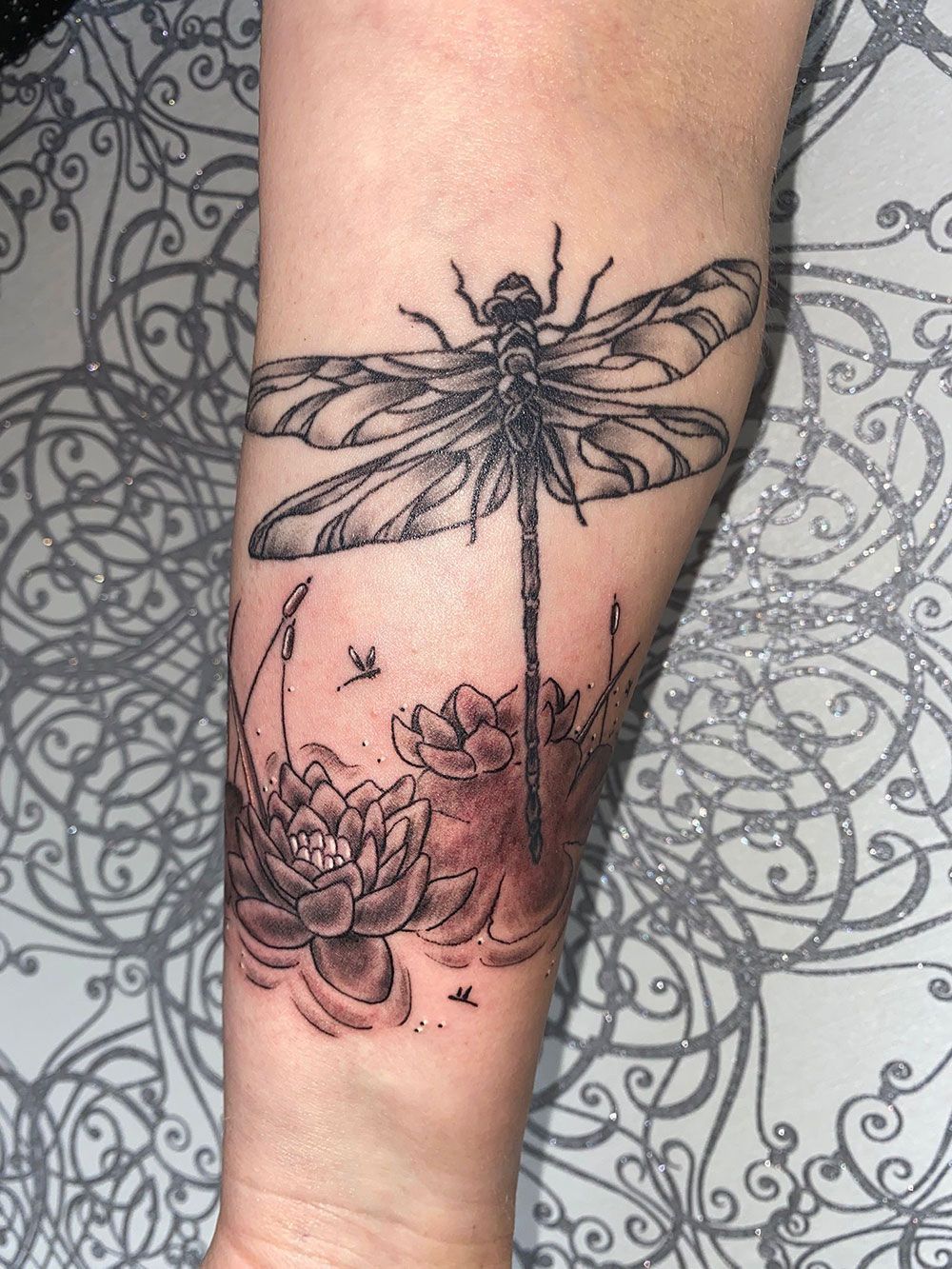 Eine Frau hat eine Libellentätowierung auf ihrem Unterarm.