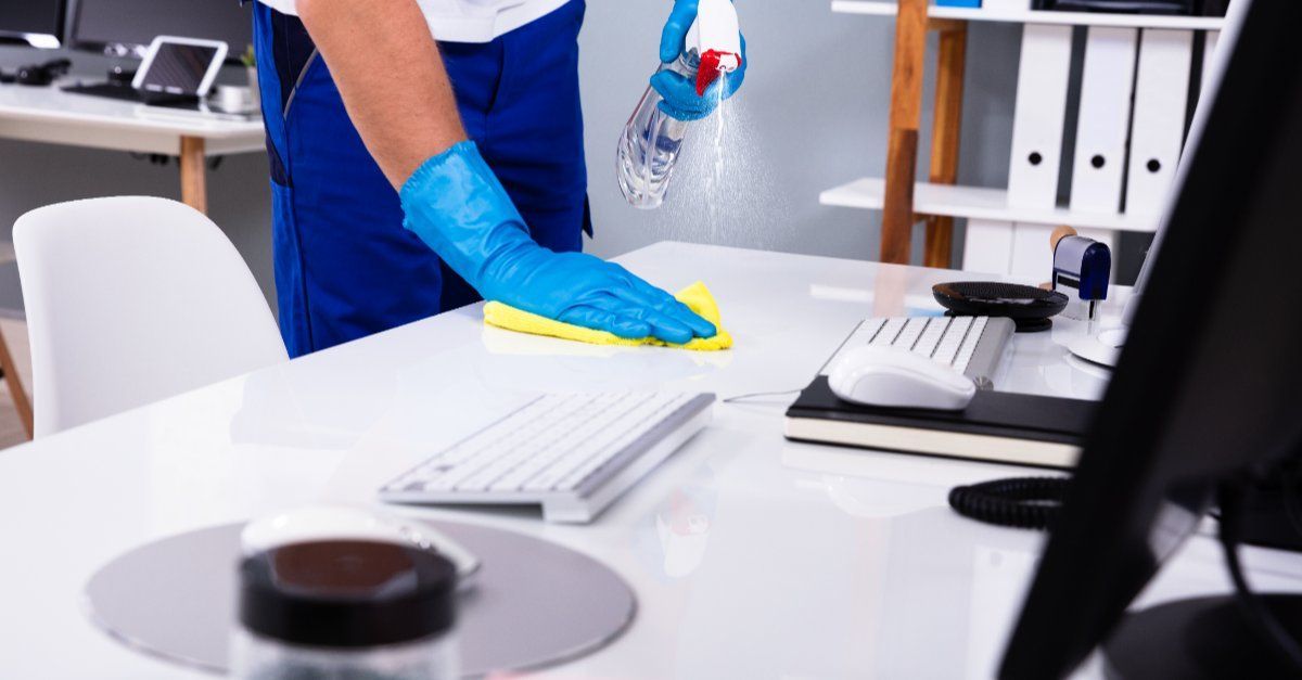 Una persona está limpiando un escritorio con una botella de spray y una esponja.