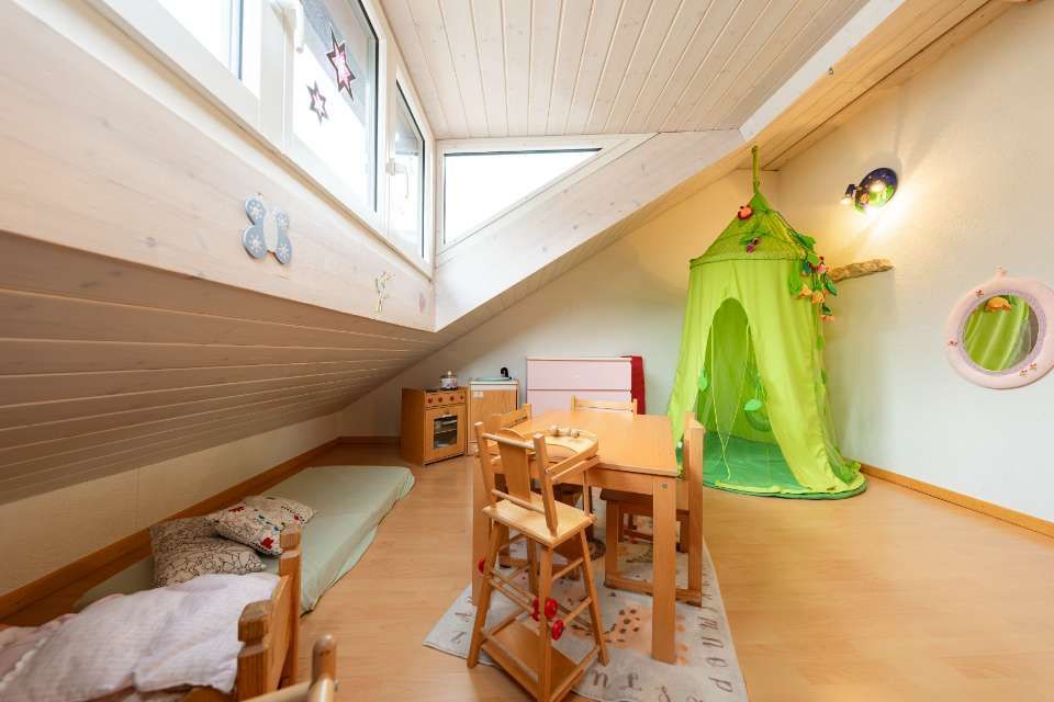 Spielzimmer mit Dachschräge; helle Holzmöbel, grünes Baldachin, Fenster und kleiner Teppich.